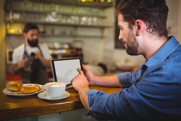 Man sitting at counter and using digital tablet while having coffee in cafÃ©