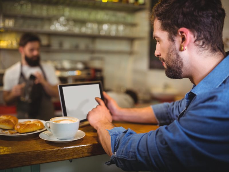 Man sitting at counter and using digital tablet while having coffee in cafÃ©